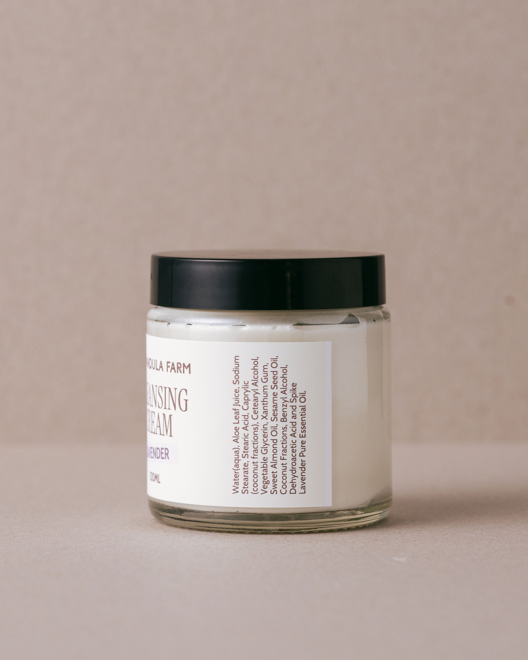 glass jar of lavender ceansing cream with a black lid on a beige background