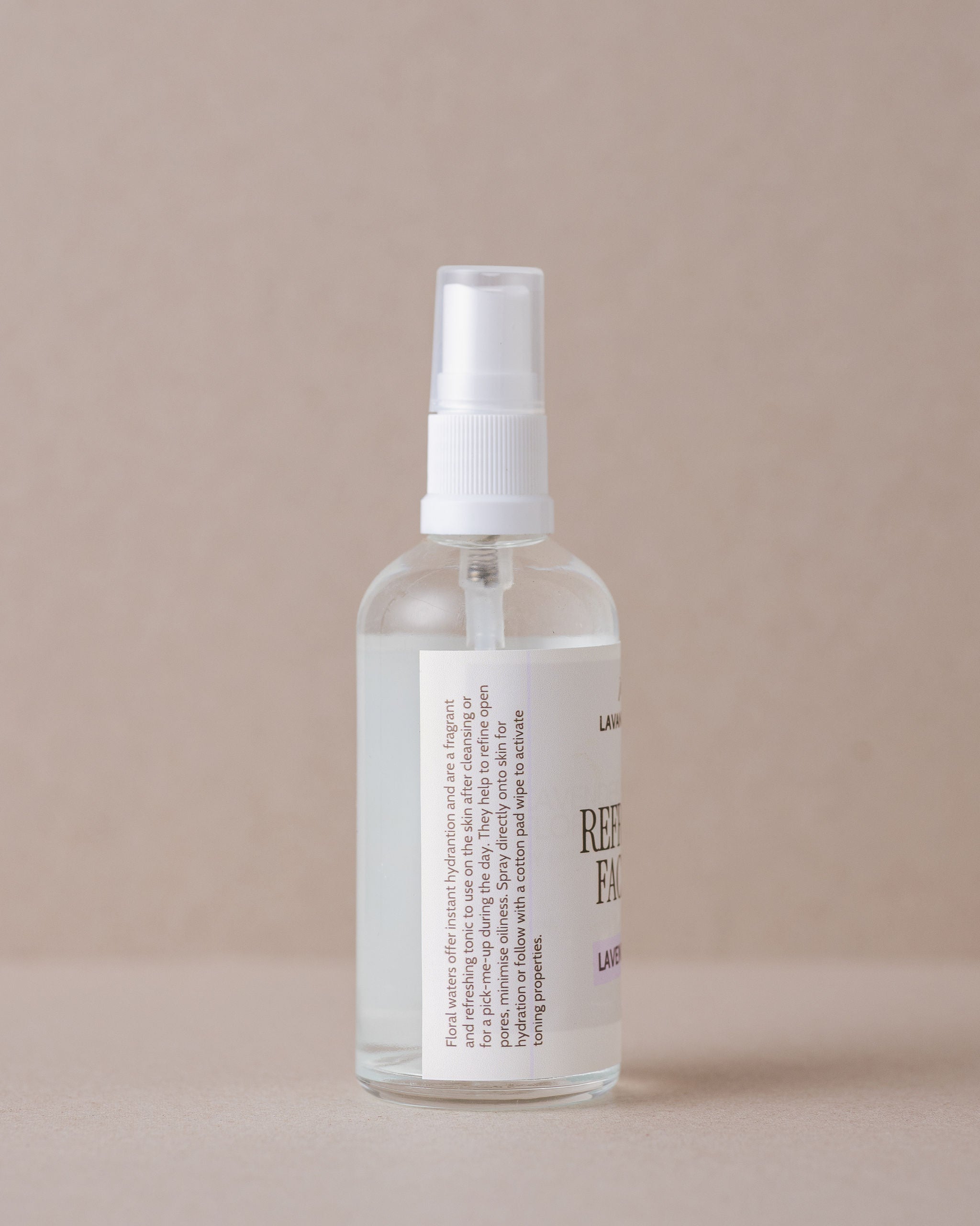 Clear spray bottle with white label on a beige background