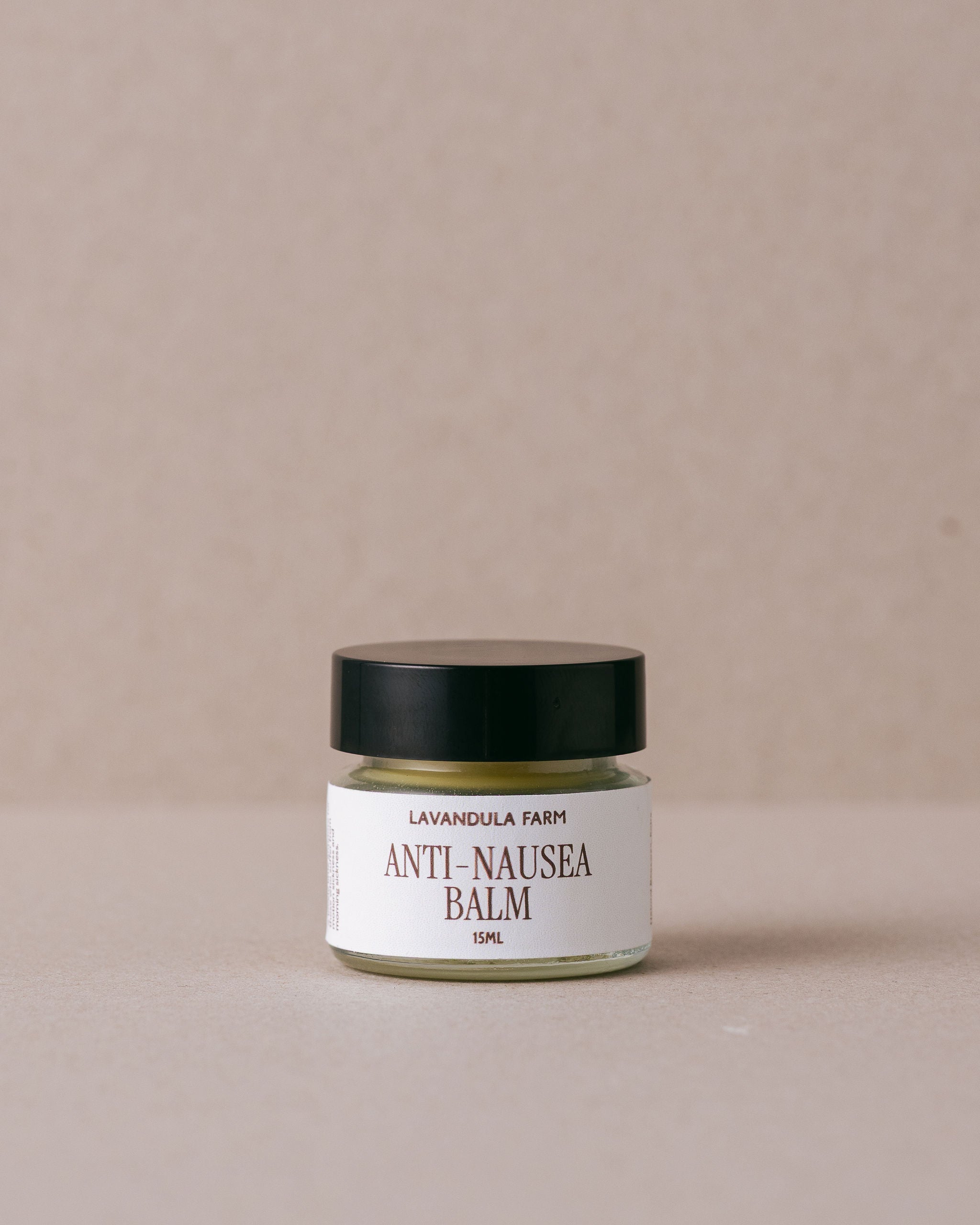 Jar of Anti-Nausea Balm with a black lid on a beige background