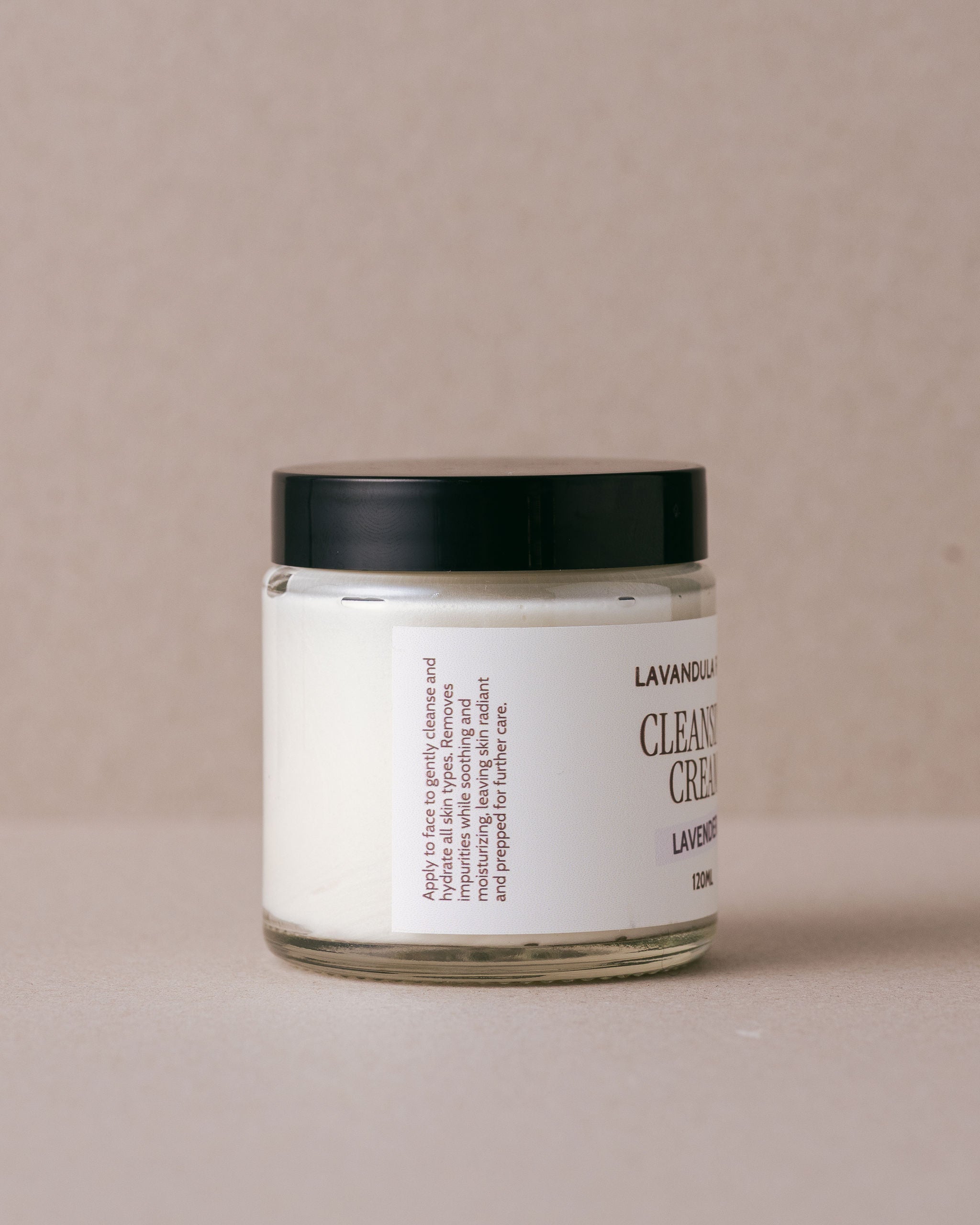 glass jar of lavender ceansing cream with a black lid on a beige background