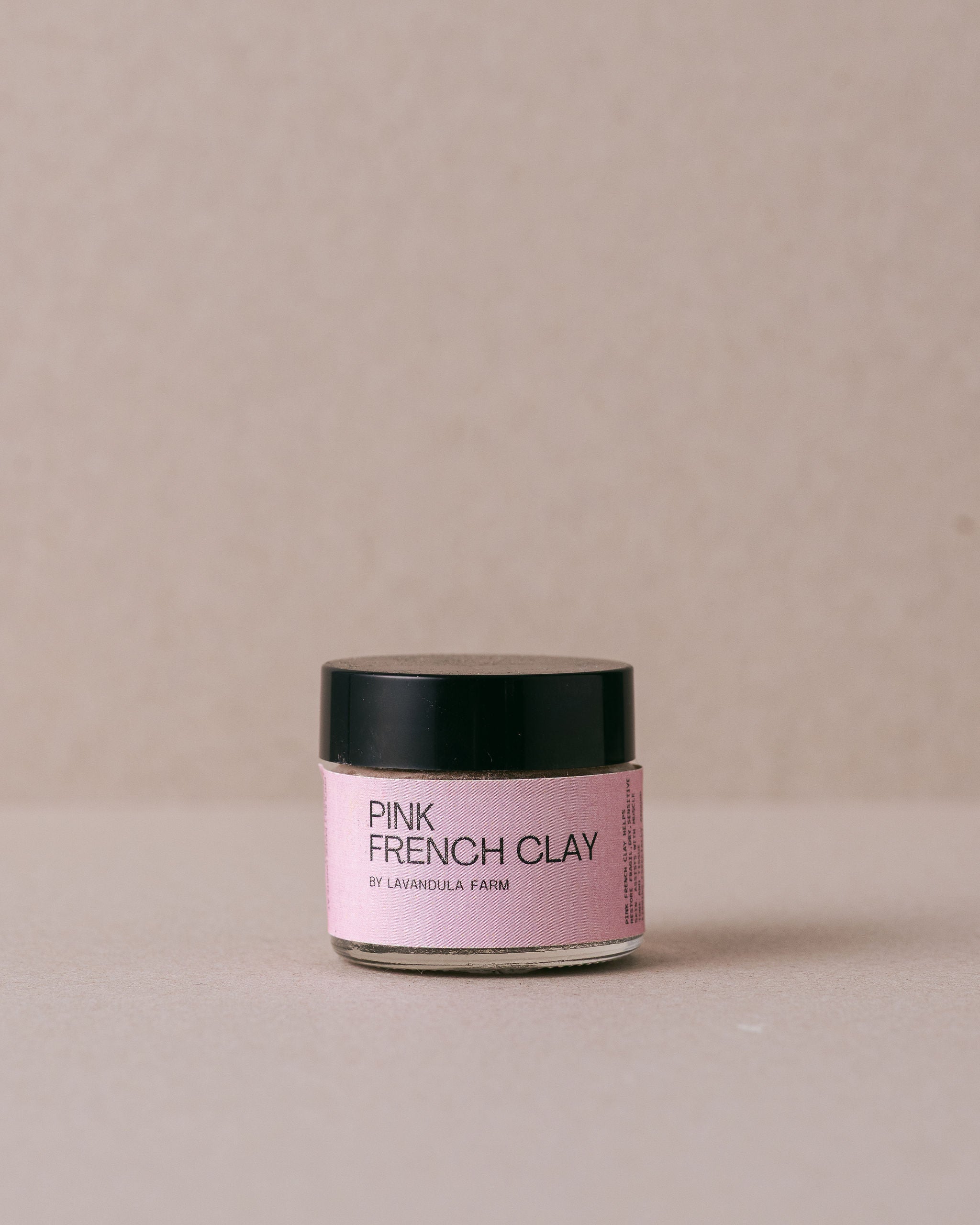 small glass jar of pink french clay on a beige background