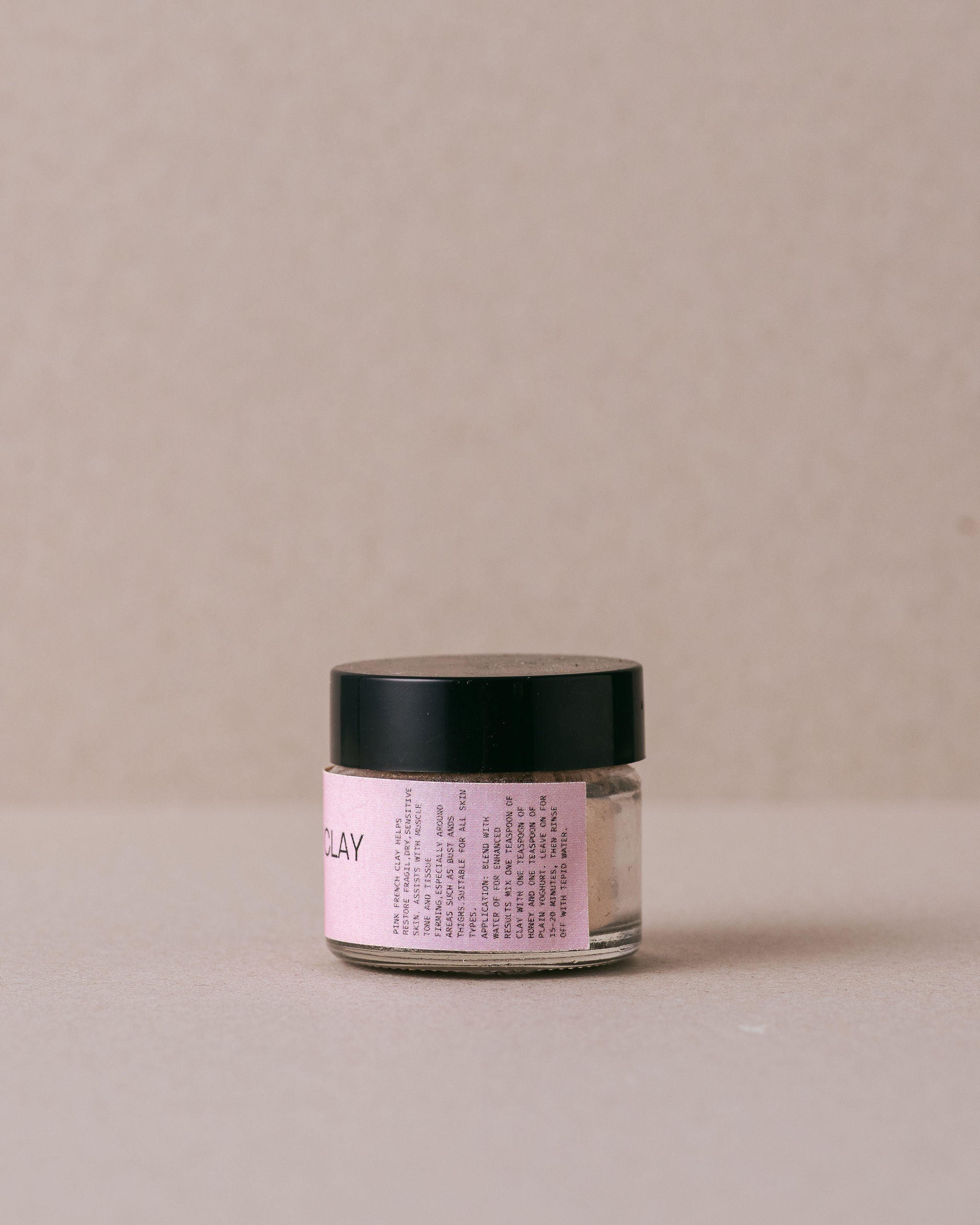 small glass jar of pink french clay on a beige background