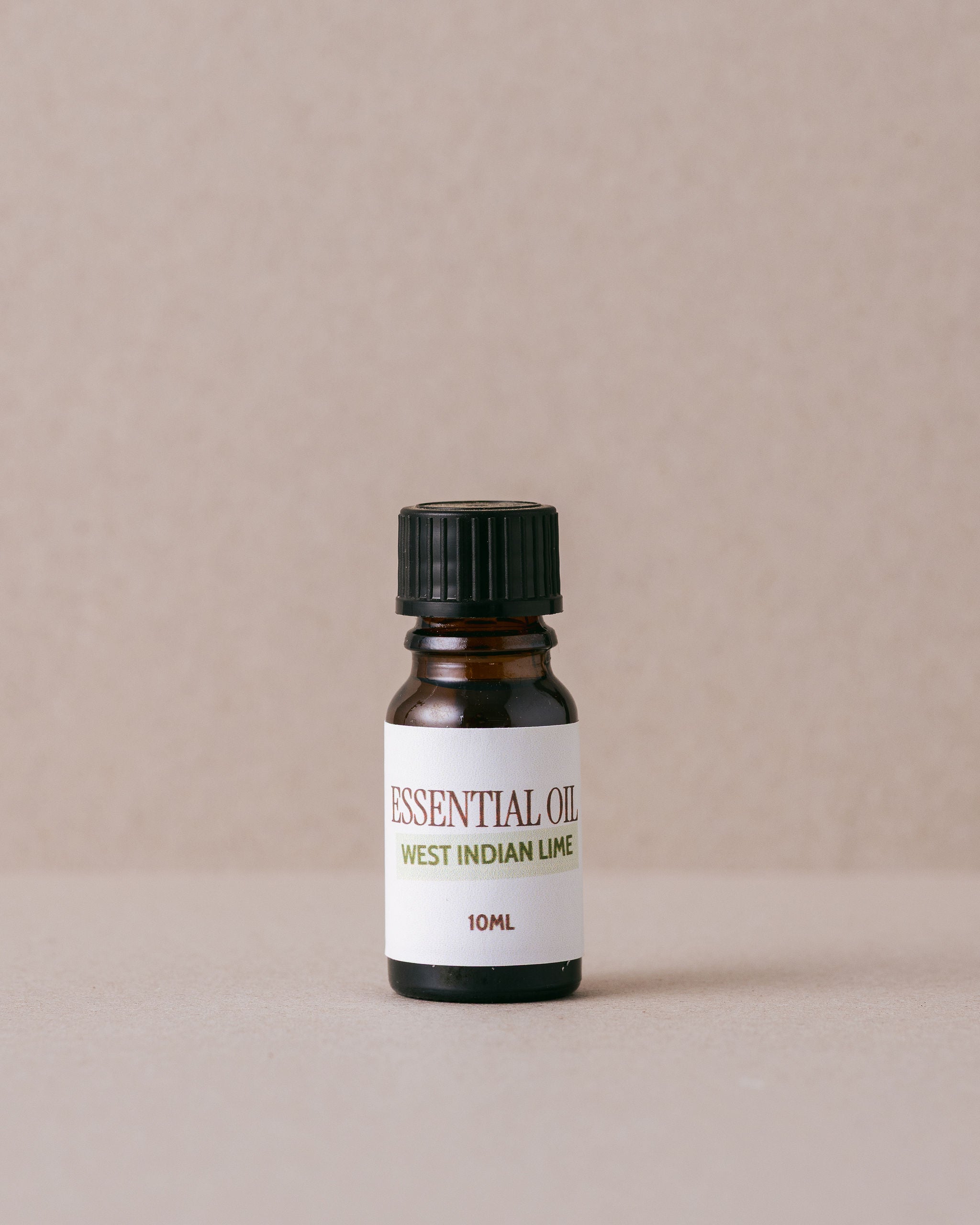 small glass essential oil bottle of west indian lime on a beige background